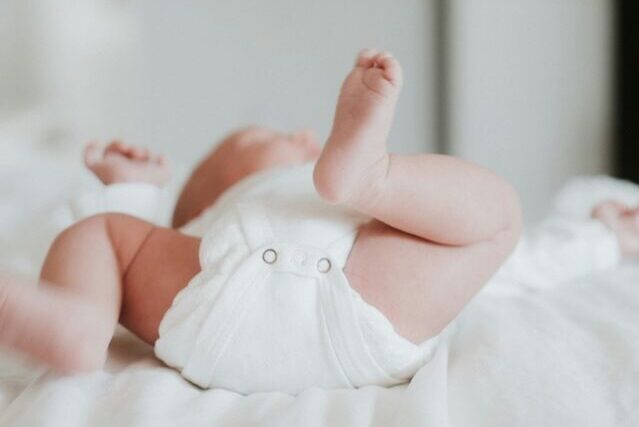 Image of baby in white onsie laying down on bed