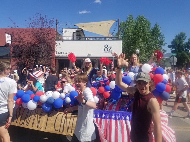 a group of people at a parade holding a sign with red, white and blue balloons