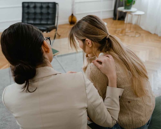 A woman comforting an adolescent girl by sitting next to her and holding her shoulder