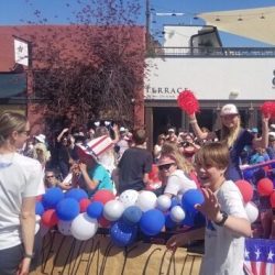 a group of people at a parade with red, white and blue balloons